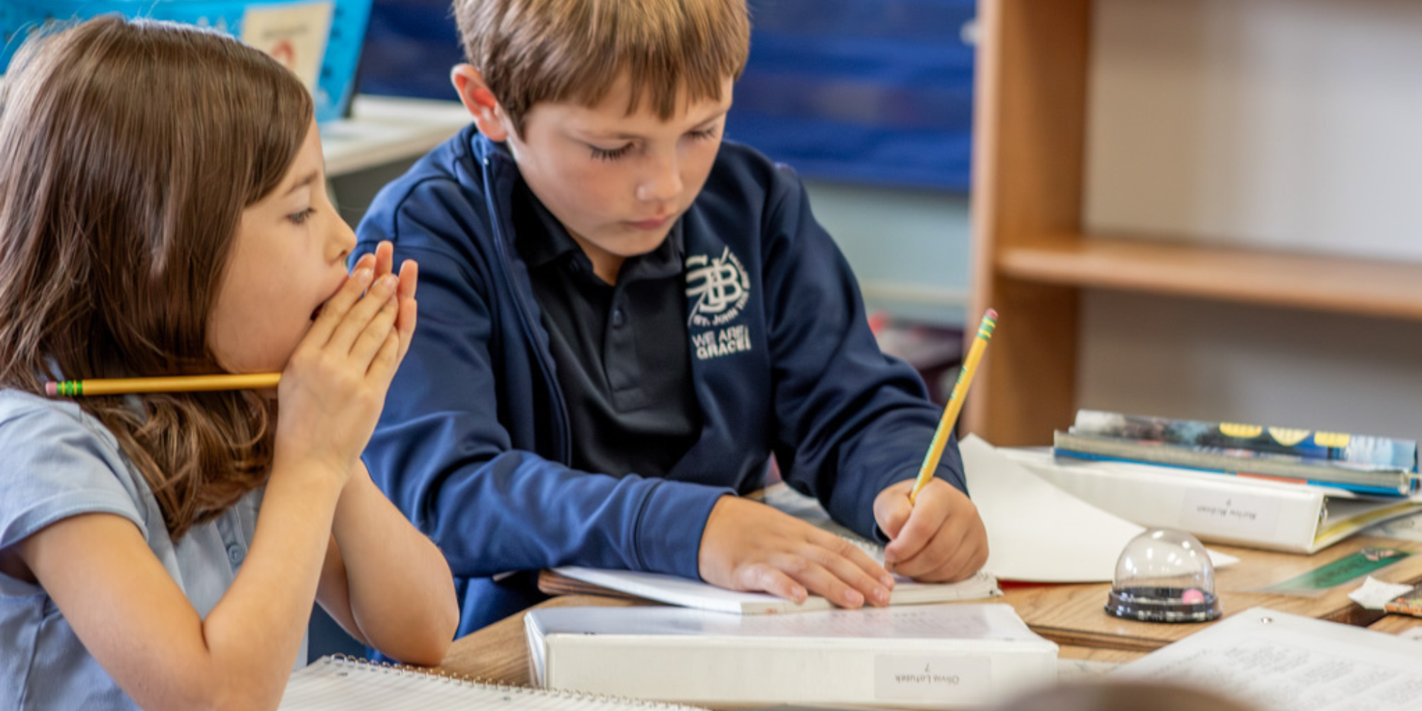 Girl and boy in St. John the Baptist Catholic School uniforms writing at desk